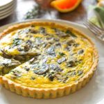 Spinach Artichoke Quiche with a slice cut out on a white plate with silver forks in the background