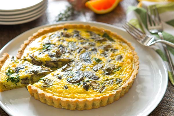Spinach Artichoke Quiche with a slice cut out on a white plate with silver forks in the background