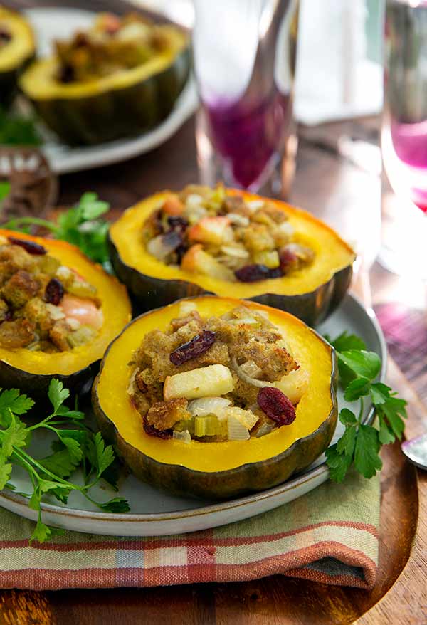 Stuffed Acorn Squash halves on a white plate with an orange plaid napkin underneath on a wooden tray