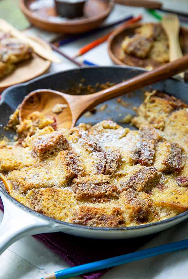 Sunbutter and Jelly Bread Pudding in a white cast iron skillet with a wooden serving spoon