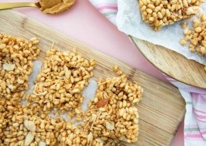 Toasted Coconut Rice Crispy Bars on a light wooden cutting board on a baby pink background