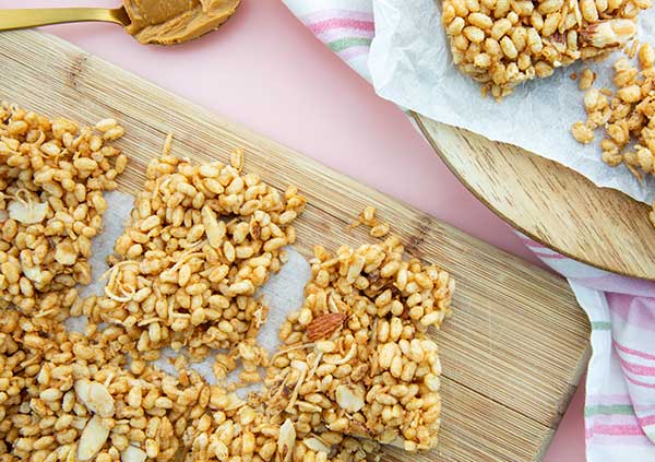 Toasted Coconut Rice Crispy Bars on a light wooden cutting board on a baby pink background