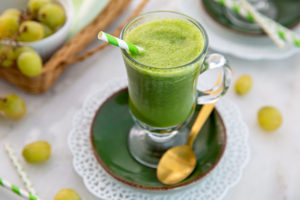 Overhead view of Mango Ginger Kale Smoothie with a green and white straw and green grapes in the background