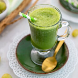 Overhead view of Mango Ginger Kale Smoothie with a green and white straw and green grapes in the background