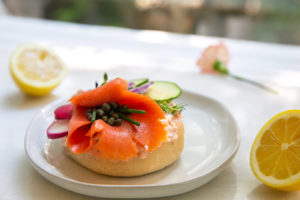 Bagels with Smoked Salmon Schmear topped with smoked salmon and capers on a white plate