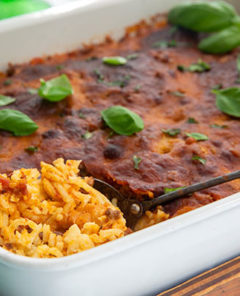 Baked Spaghetti in a white rectangle baking dish topped with basil leaves
