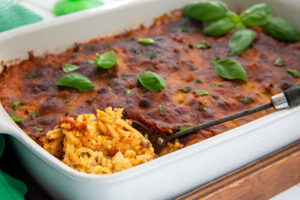 Baked Spaghetti in a white rectangle baking dish topped with basil leaves