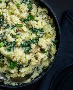 Overhead view of Cauliflower Colcannon in a dark blue bowl on a black background