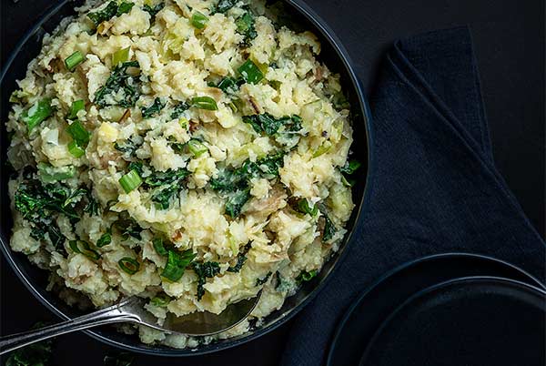 Overhead view of Cauliflower Colcannon in a dark blue bowl on a black background