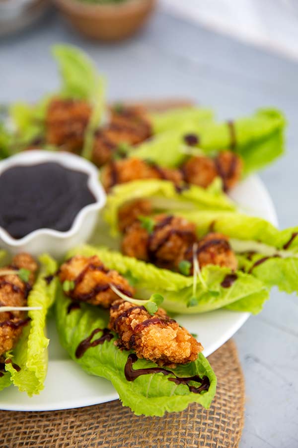 Closeup of Chicken Lettuce Wraps with sauce drizzled over top on a white plate with ramekin of sauce in the center