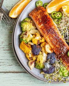 Chili-Crusted Salmon Bowl arranged artfully on a plate with orange slices on a light wood background