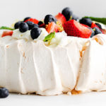Closeup of Classic Pavlova topped with fresh berries and mint on a white background
