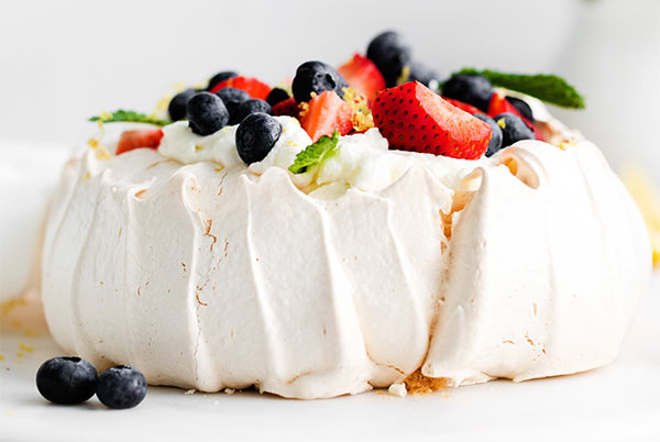 Closeup of Classic Pavlova topped with fresh berries and mint on a white background