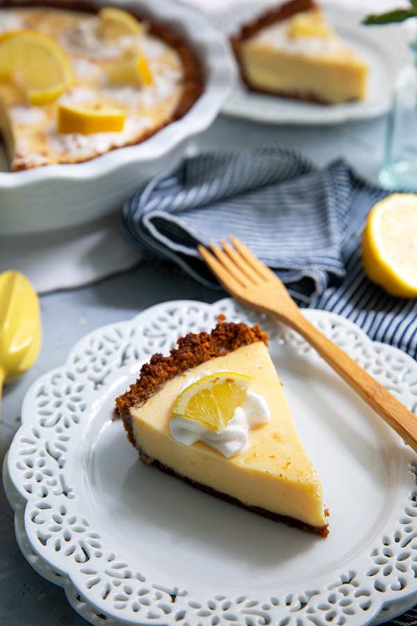 Slice of Creamy Lemon Pie on a white ceramic plate with decorative edges and a slice of lemon on top
