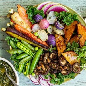 Crispy Veggies with Kale-Honey Pesto arranged artfully in a bowl with a small dish of cheese and pesto on the side on a faded wood background
