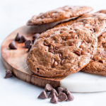 Flourless Chocolate Cookies on a round marble and wood serving board with chocolate chips scattered around