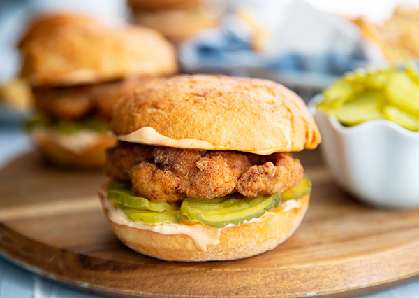Closeup of a Fried Chicken Sandwich with pickles on a round wooden serving board