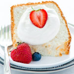 Gluten-Free Angel Food Cake slice on a white plate topped with whipped cream and fresh strawberries