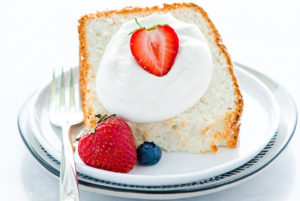 Gluten-Free Angel Food Cake slice on a white plate topped with whipped cream and fresh strawberries