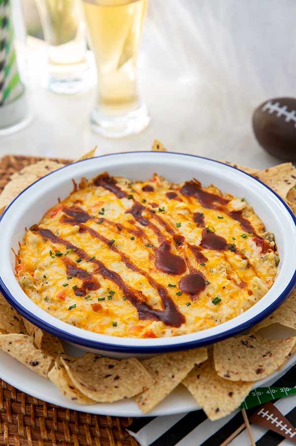 Hot Hatch Chili and Crab Dip in a white bowl with tortilla chips around it and football decorations in the background