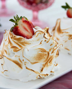 Individual Baked Alaskas topped with fresh strawberries on a white platter with pink tablecloth and pink glasses in the background