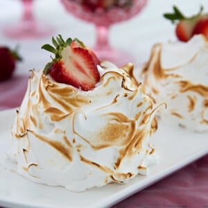 Individual Baked Alaskas topped with fresh strawberries on a white platter with pink tablecloth and pink glasses in the background