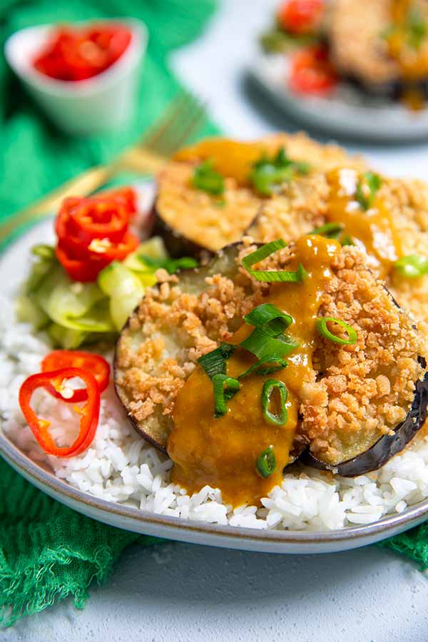 Katsu Curried Eggplant on a bed of white rice topped with green onions and red chilies on an emerald green napkin
