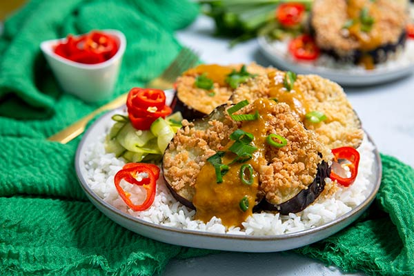 Katsu Curried Eggplant on a bed of white rice with red chilies on top on an emerald green cloth napkin