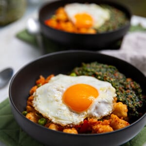 Korean Fried Rice with Cilantro Sauce topped with a fried egg in a black bowl on a sage green placemat