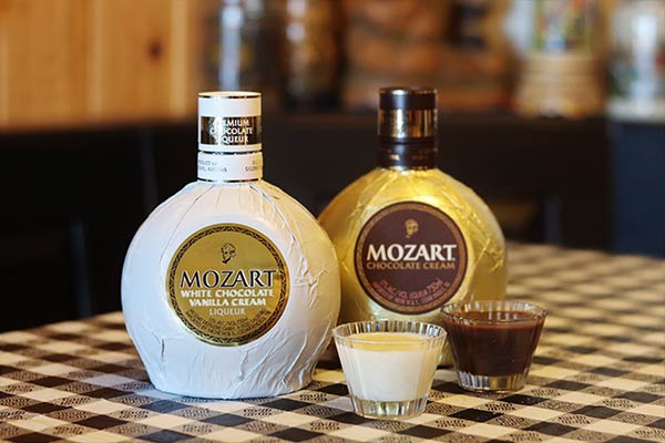Bottles of Mozart White Chocolate and Chocolate Cream Liqueurs on a white and black checkered tablecloth with shots of each in front