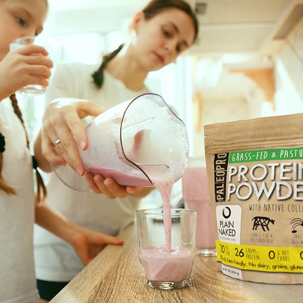 Paleo Pro Strawberry Protein Shake being poured from the blender into a glass with a woman and her daughter in the background