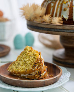 Pistachio Lemon Cake slice on a brown wooden plate with the remaining cake on a wooden platter in the background