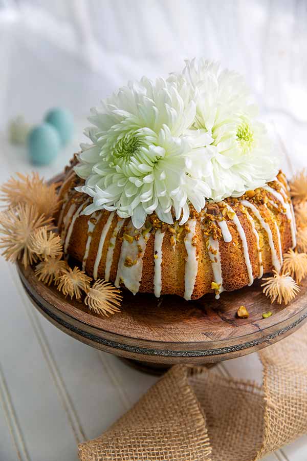 Pistachio Lemon Cake with big white flowers on top as decoration sitting atop a wooden cake pedestal