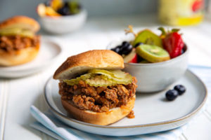 Sloppy Joes on a white plate with fresh sliced fruit in the background