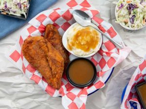 Overhead view of Southern Fry'd Chicken with mashed potatoes and gravy in a basket with red and white checkered paper in it