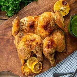 Overhead view of Spatchcock Chicken with Salsa Verde on a wooden cutting board with blue and white napkin and plates
