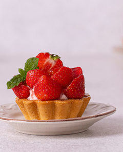 Strawberry Tartlet loaded with fresh strawberries and a garnish of mint leaves on a white plate with white background