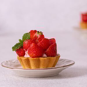 Strawberry Tartlet loaded with fresh strawberries and a garnish of mint leaves on a white plate with white background