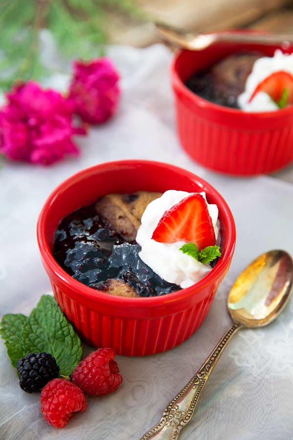 Overhead view of Sunbutter and Jelly Mug Cakes in red ramekins with fresh berries and mint on the side on a white lace tablecloth
