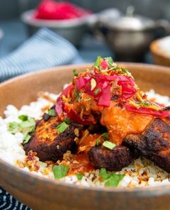 Closeup of Tandoori Tikka Chicken topped with pickled red onion in a beige bowl with dark blue napkin and background