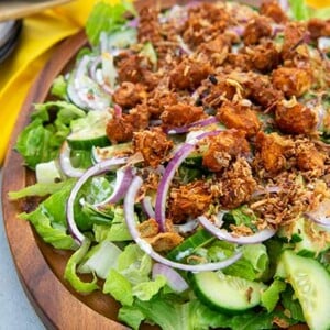 Tandoori Tikka Chicken Salad on a wooden serving plate with yellow napkin underneath