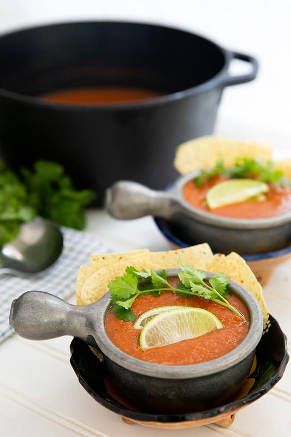 Closeup of two bowls of Tomato Tortilla Soup in silver bowls with a black pot of soup in the background