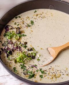 Vegan Alfredo Sauce in a skillet with a wooden spoon in the sauce and topped with fresh microgreens