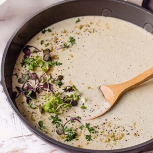 Vegan Alfredo Sauce in a skillet with a wooden spoon in the sauce and topped with fresh microgreens
