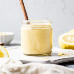 Vegan Hollandaise Sauce in a clear glass jar with halved lemons in the background