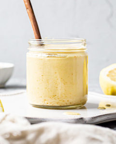 Vegan Hollandaise Sauce in a clear glass jar with halved lemons in the background