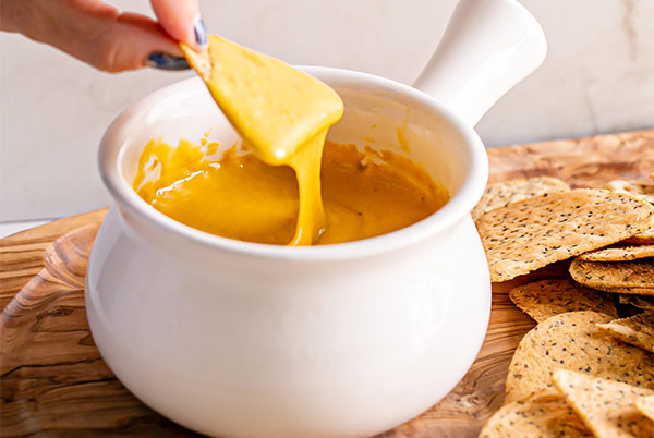 Vegan Nacho Cheese Sauce in a white fondue bowl with a chip being dipped into it