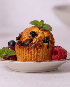 Very Berry Muffins garnished with fresh berries and mint leaves on a white plate with white background
