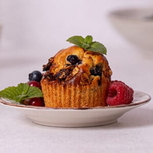 Very Berry Muffins garnished with fresh berries and mint leaves on a white plate with white background