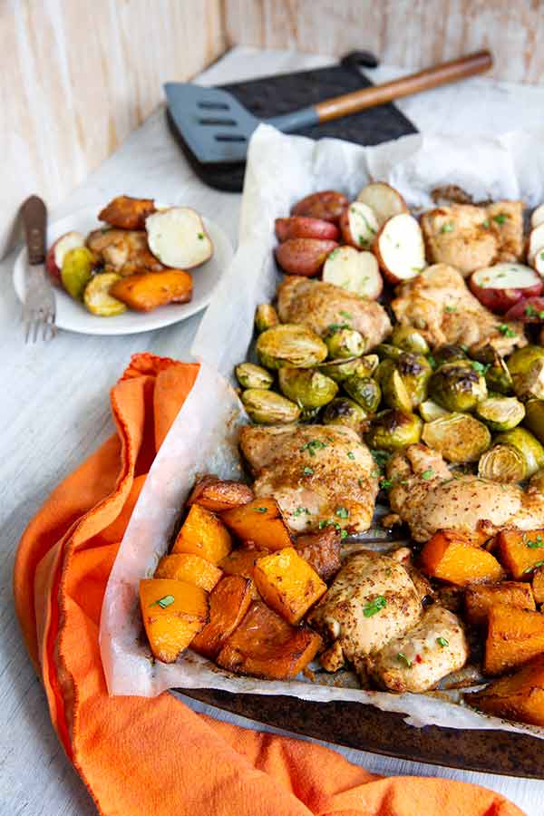 Chicken and Veggies Sheet Pan Dinner on a parchment lined baking sheet with an orange cloth napkin underneath